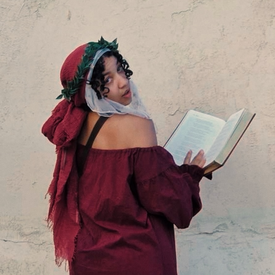The artist wearing an off-shoulder red blouse, red headdress and crown of laurels, looking back at the viewer while holding a book, The Divine Comedy